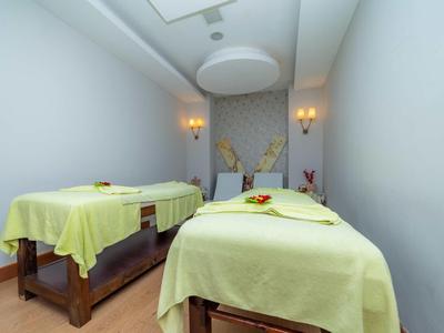 Stanza spa tranquilla con due lettini da massaggio coperti da lenzuola verde chiaro e luce soffusa.