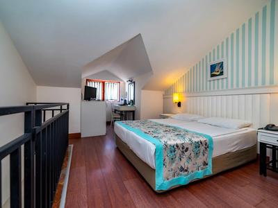 Camera mansardata accogliente con letto matrimoniale, pavimento in legno, pareti a strisce e lampade da comodino.