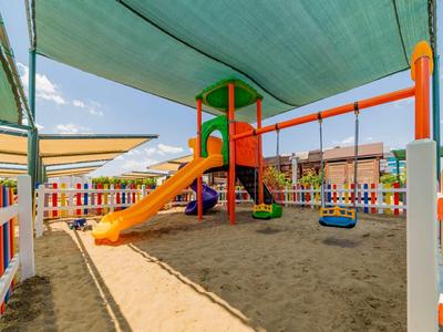 Parco giochi colorato con scivolo e altalene coperto da una vela ombreggiante sulla sabbia.