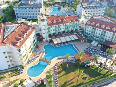 Vista aerea di un hotel con una grande piscina all'aperto, lettini e edifici circostanti.