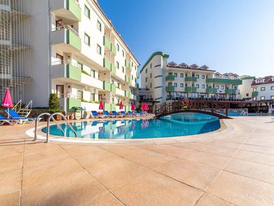 Area piscina esterna dell'hotel con lettini e ombrelloni accanto a edifici multipiano sotto un cielo blu.