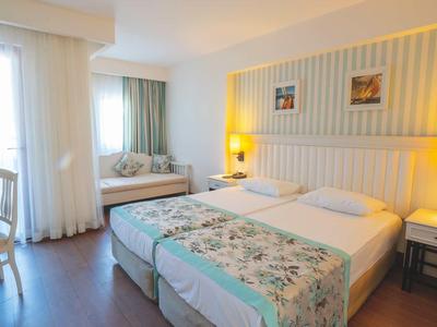 Camera d'albergo luminosa con letto matrimoniale, comodini, scrivania e ampia finestra con tende.