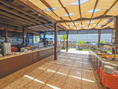 Area pranzo all'aperto coperta con tavoli buffet e vista sul mare.