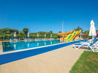 Piscina esterna con scivoli d'acqua e lettini sotto un cielo azzurro.