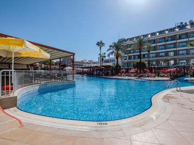 Hotelpool mit klar blauem Wasser, Sonnenliegen und Hotelgebäude bei sonnigem Himmel.