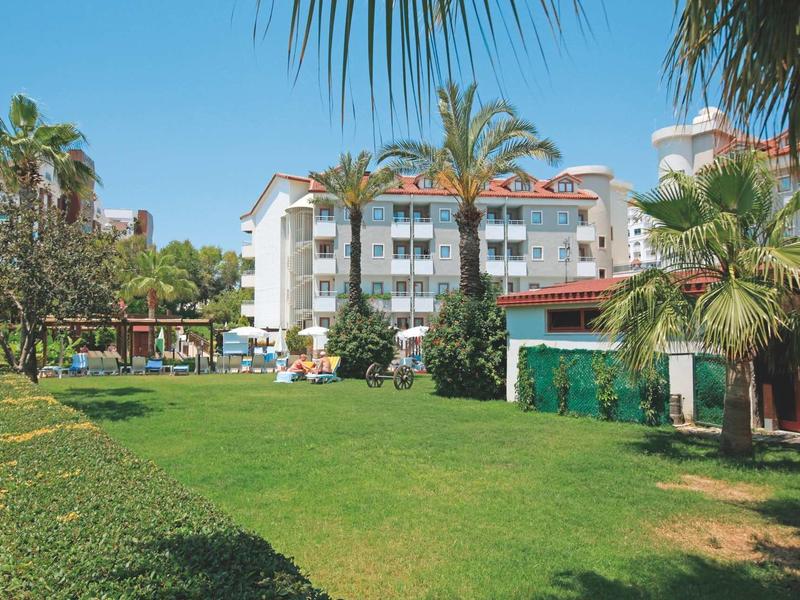 Edificio dell'hotel con balconi, prato verde, palme e cielo azzurro soleggiato