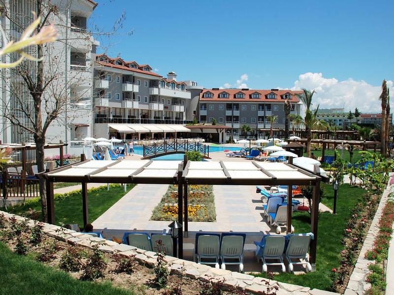 Area piscina con lettini, ombrelloni e un grande edificio dell'hotel sullo sfondo in una giornata di sole.