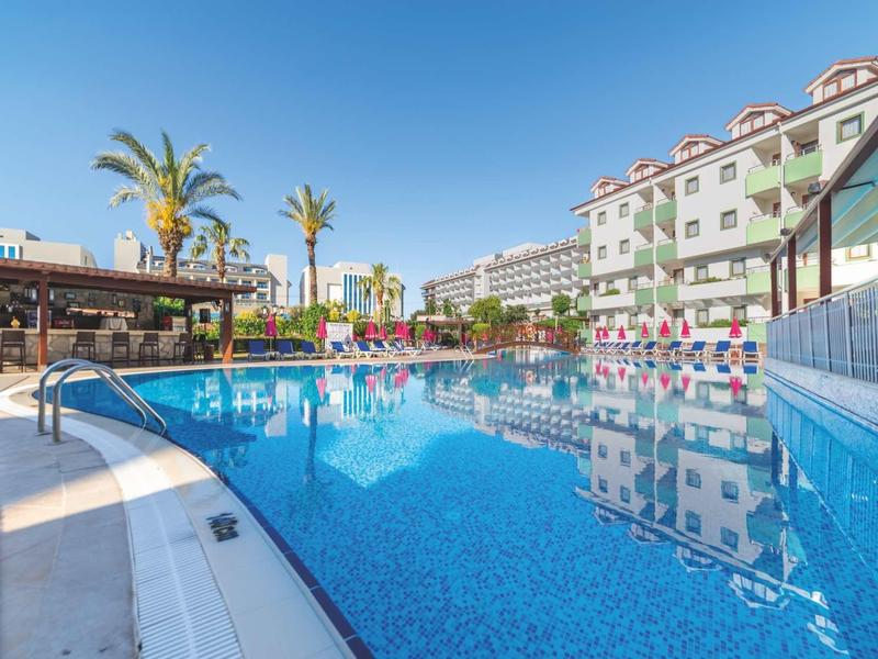 Piscina all'aperto dell'hotel con acqua blu chiara e palme sotto un cielo soleggiato.
