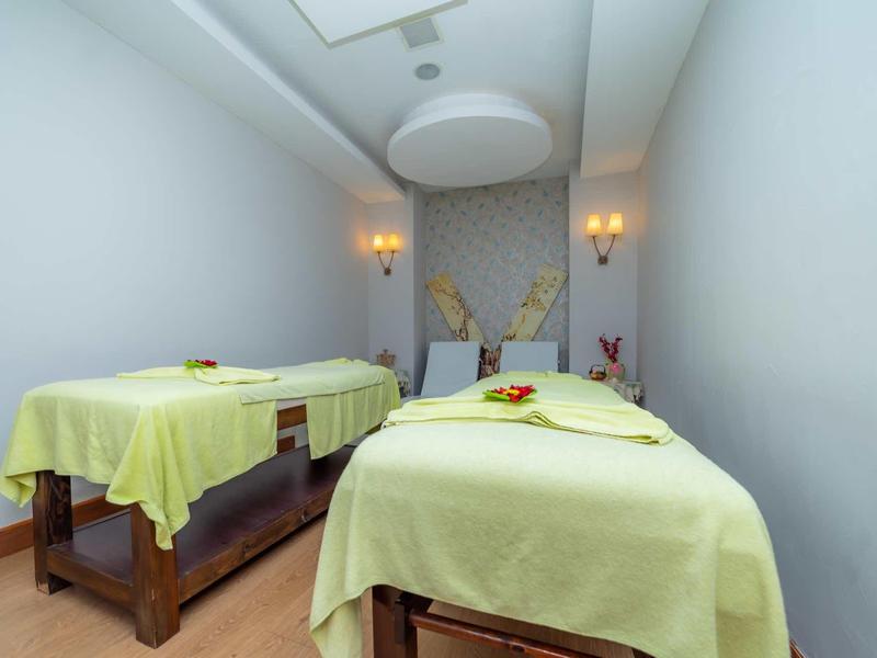 Stanza spa tranquilla con due lettini da massaggio coperti da lenzuola verde chiaro e luce soffusa.