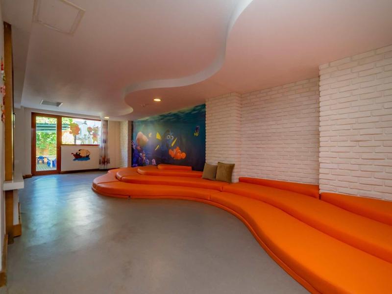 Seduta curva arancione con cuscini in una stanza spaziosa con parete in mattoni bianchi e grande finestra.