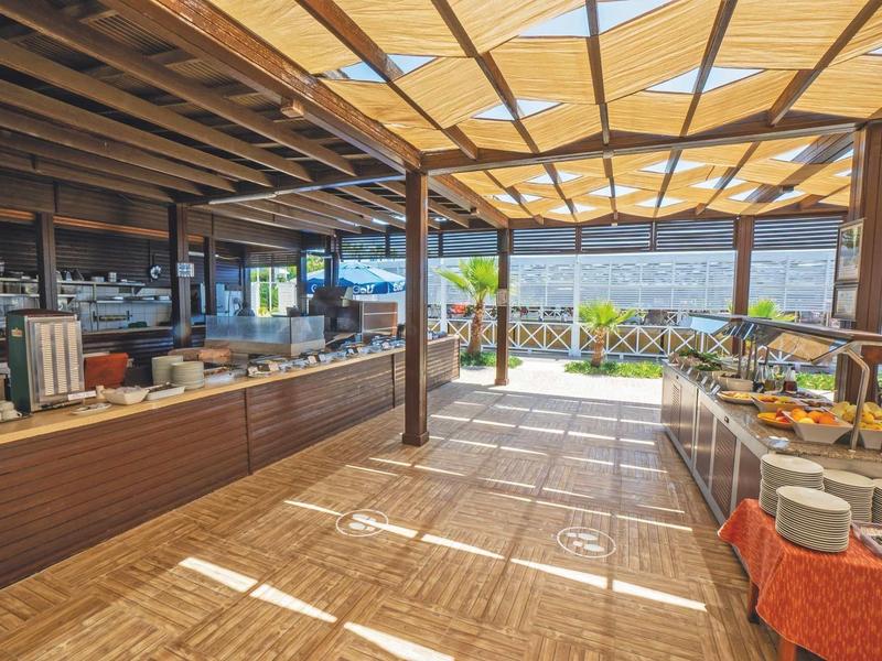 Area pranzo all'aperto coperta con tavoli buffet e vista sul mare.