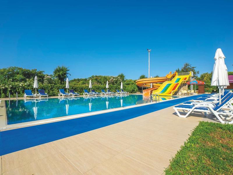 Piscina esterna con scivoli d'acqua e lettini sotto un cielo azzurro.