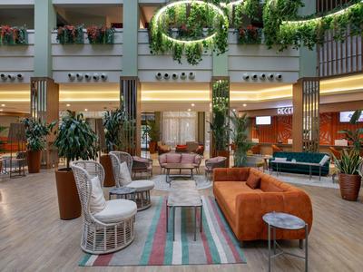 Ampia hall d'hotel moderna con varie zone salotto e molta vegetazione.