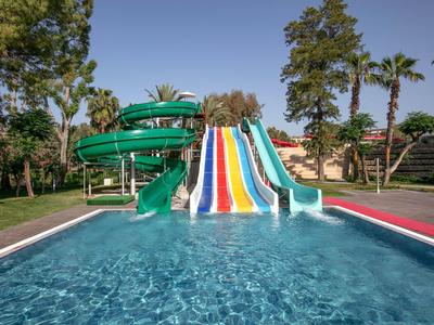 Vodní park s barevnými skluzavkami a točitým skluzem do bazénu obklopeného stromy.