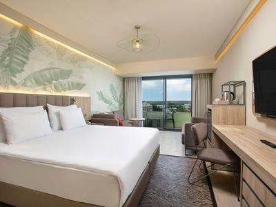 Moderní hotelový pokoj s velkou postelí, psacím stolem, televizí a velkým oknem s výhledem.