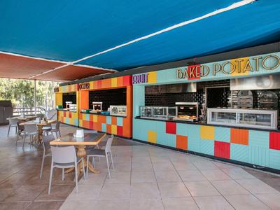 Barevné venkovní stánky pod modrým markýzou s stoly a židlemi na dlažbě