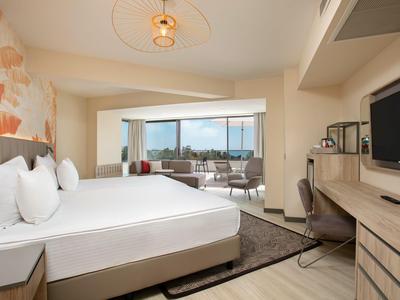 Moderní hotelový pokoj s velkou postelí, pracovním stolem a balkonem s výhledem na město.