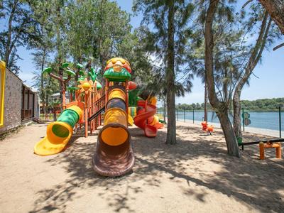 Dětské hřiště s barevnými trubkovými skluzavkami u jezera pod stromy.