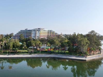 Velká vícepatrová hotelová budova vedle klidné vody se zeleným břehem.