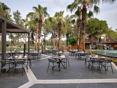 Venkovní restaurace se stoly a židlemi obklopená palmami a bazénem.