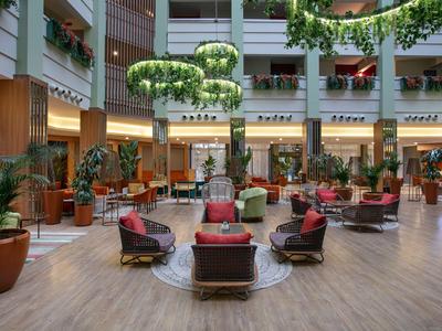Prostorná hotelová lobby s křesly, rostlinami a závěsnými zelenými dekoracemi.