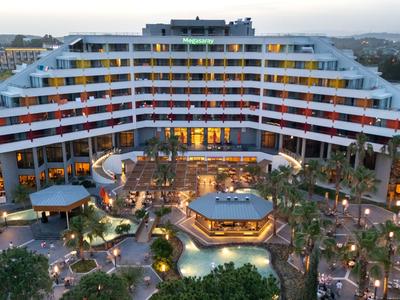 Moderní velký hotel s několika patry, bazénem a palmami v upravené oblasti.