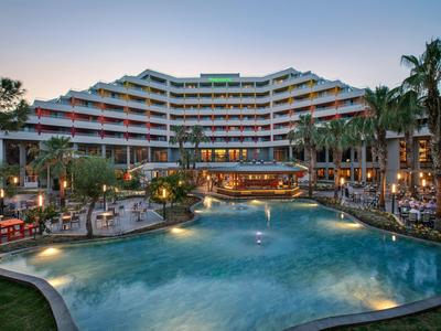 Luxusní hotel s velkým venkovním bazénem, palmami a osvětlenou terasou za soumraku.