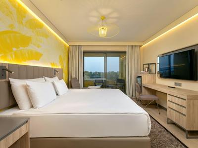 Moderní hotelový pokoj s velkou postelí, TV a balkonem s výhledem.