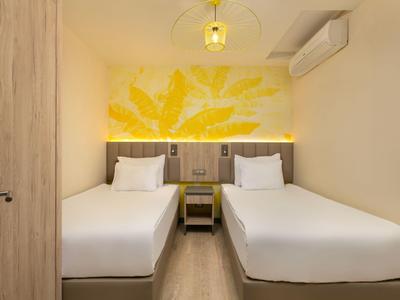Pokoj se dvěma jednolůžky, žlutou dekorací na stěně a moderním osvětlením