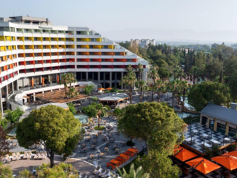 Moderní hotel s barevnými balkonky, obklopený zelenými stromy a venkovním bazénem.