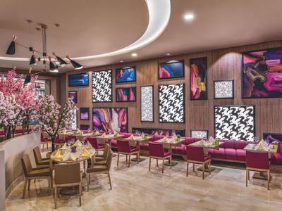 Nowoczesna restauracja hotelowa z wygodnymi krzesłami, kolorową sztuką i kwitnącymi roślinami.