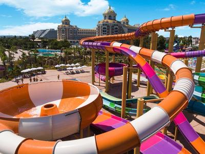 Scivoli d'acqua colorati che si intrecciano in un parco acquatico sotto un cielo azzurro con castelli sullo sfondo.