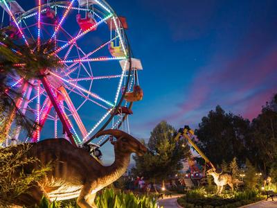 Dinosauri e una ruota panoramica illuminata di notte in un parco divertimenti.