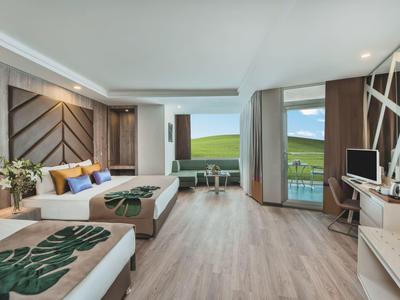 Camera d'hotel luminosa con due letti, pavimento in legno e grande finestra con vista sulle colline verdi.