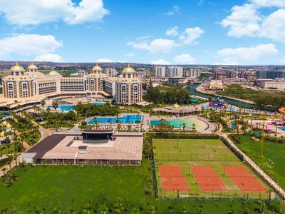 Grande resort con piscine, campi da tennis e aree esterne sotto un cielo azzurro.