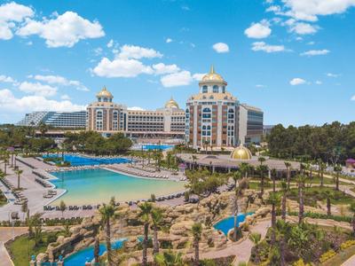 Large hotel with pool and palm trees under blue sky in a vacation resort.