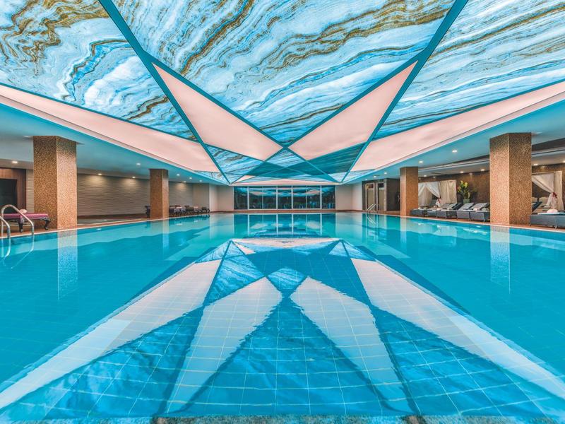 Piscina interna con acqua blu e luci artistiche sul soffitto in un hotel moderno.