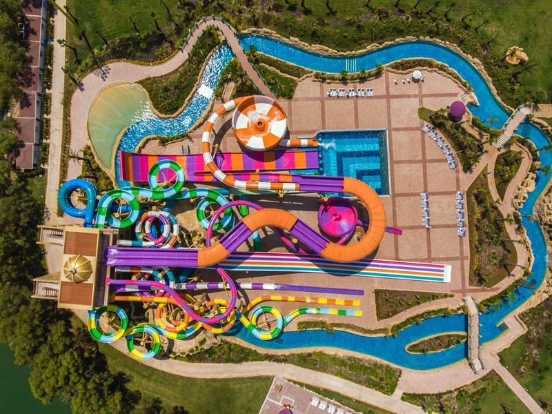 Vista aerea di un parco acquatico colorato con molteplici scivoli e un fiume lento.