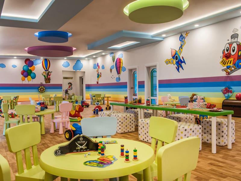 Sala giochi colorata per bambini con tavoli, sedie, giocattoli e decorazioni murali.