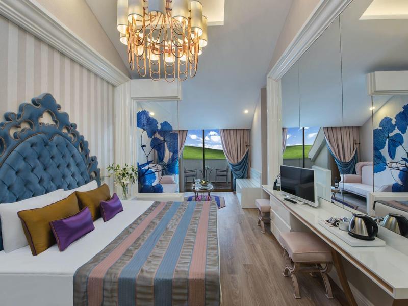 Camera d'hotel elegante con testiera blu capitonnè, lampadario, scrivania e balcone.
