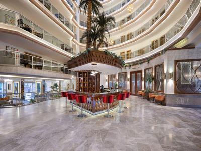 Großer heller Lobbybereich mit Palmen, Bar in der Mitte, roten Stühlen und glänzendem Marmorfußboden.