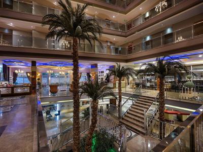Innenraum eines modernen Einkaufszentrums mit Palmen, Treppen und mehrstöckigen Glasgeländern.