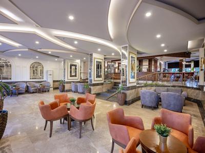 Moderner Hotel-Loungebereich mit runden Tischen, bunten Sesseln, Theke und heller Deckenbeleuchtung.