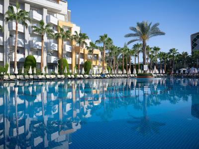 Grande piscina davanti a un hotel con palme e cielo azzurro.