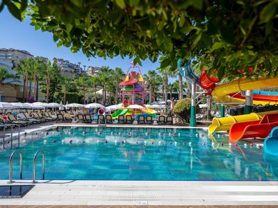 Großes Schwimmbecken mit Wasserrutschen, Sonnenliegen und Palmen unter blauem Himmel.