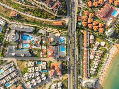 Luftaufnahme von Wohnanlagen mit Pools, Straßen und Strand am Meer rechts neben der Bebauung.
