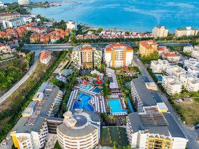 Luftaufnahme eines großen Hotels mit Pool, umgeben von Straßen, Wohnungen und Meer im Hintergrund.