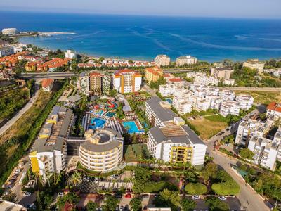 Küstenstadt mit modernen Wohngebäuden, Pools und grünem Umfeld am blauen Meer unter klarem Himmel.