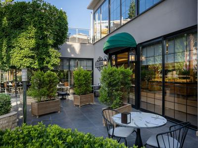 Moderner Hotelterrassenbereich mit Tischen, Stühlen, Pflanzen und einer glasverkleideten Fassade.