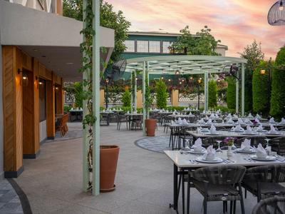 Große Terrasse mit gedeckten Tischen, Pergola, Keramikvasen und Hecken bei Sonnenuntergang.